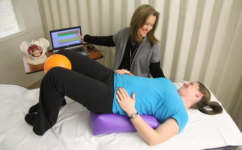 Patient lying on a structure receiving pelvic floor exercise assistance from a doctor.